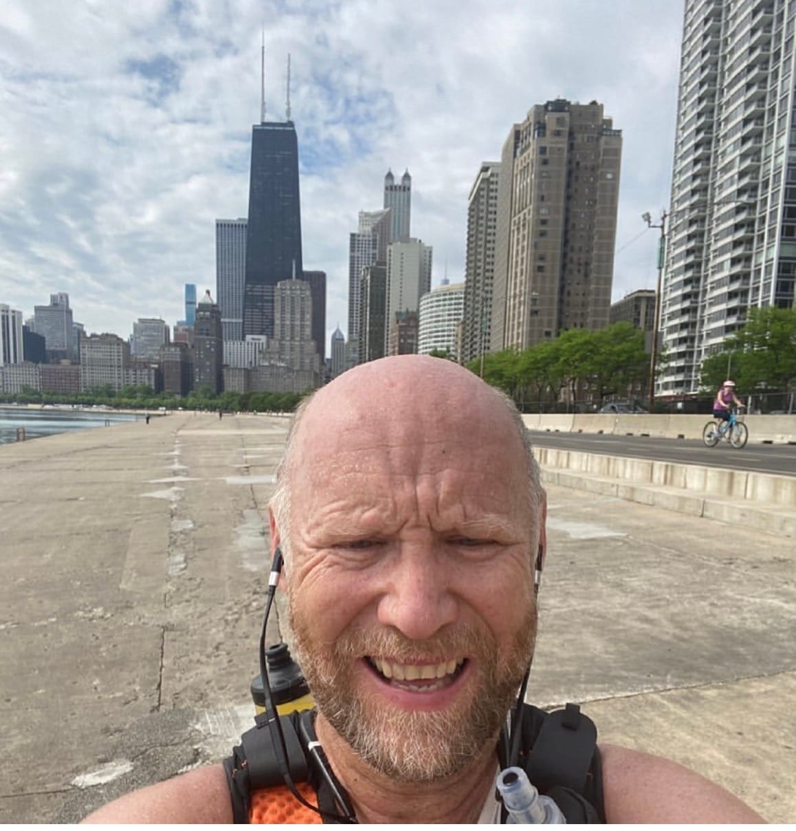 A solitary runner on the Chicago lakefront path with the John Hancock Center rising in the background and Lake Michigan on the left.